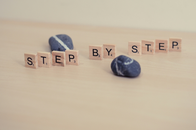 Træklodser, der staver STEP BY STEP, ved siden af en mørk sten